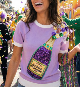 Person wearing a Mardi Gras-themed shirt with a champagne bottle design in a festive setting.