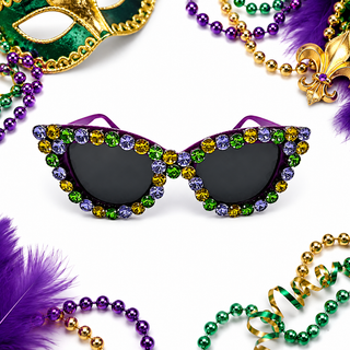 Mardi Gras themed cat-eye sunglasses adorned with purple, green, and gold rhinestones, surrounded by festive Mardi Gras beads, feathers, and a gold masquerade mask on a white background.