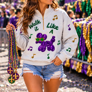 quarter-zip sweatshirt with Mardi Gras graphics, including the text 'Walk it Like a' and a purple bead dog design with green sunglasses, denim shorts, and white boots, while holding Mardi Gras beads in a festive parade setting.