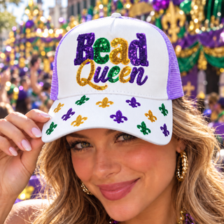 A woman wearing a white and purple trucker hat with 'Bead Queen' embroidered in Mardi Gras colors on the front, with fleur-de-lis sequins on the brim, set against a festive parade background.