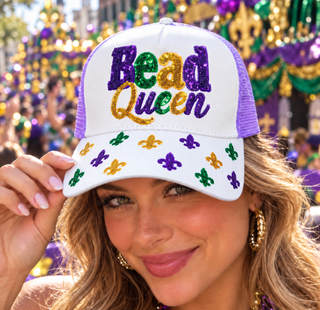 A woman wearing a white and purple trucker hat with 'Bead Queen' embroidered in Mardi Gras colors on the front, with fleur-de-lis sequins on the brim, set against a festive parade background.
