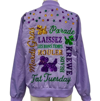 A lavender purple satin bomber jacket shown from the back, featuring colorful Mardi Gras themed sequin and glitter text including 'Mardi Gras', 'Parade', 'Laissez', 'Rouler', 'Krewe', 'Beads', and 'Fat Tuesday', with green, gold, and purple beads across the shoulders.